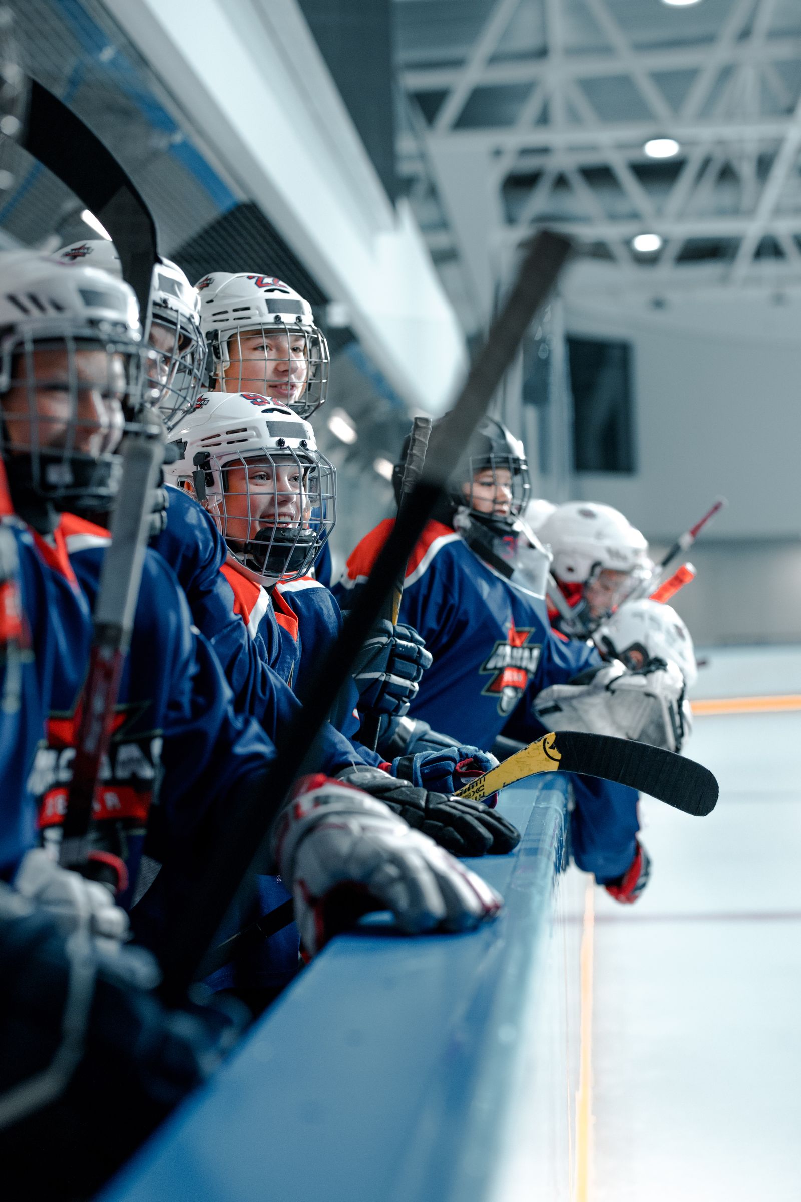 Young hockey players sit together on the rink bench during practice.